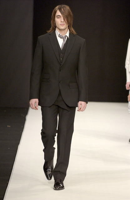 Man in a black STÆRK suit walking on a runway with a plain background