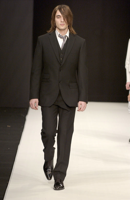 Man in a black STÆRK suit walking on a runway with a plain background