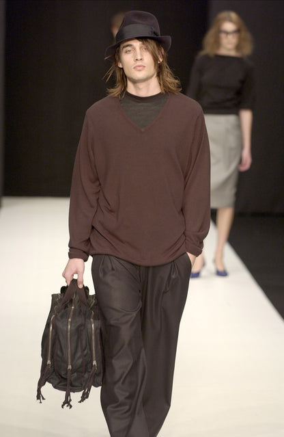 Man walking on a runway wearing a STÆRK brown and black outfit with a hat and carrying a bag.